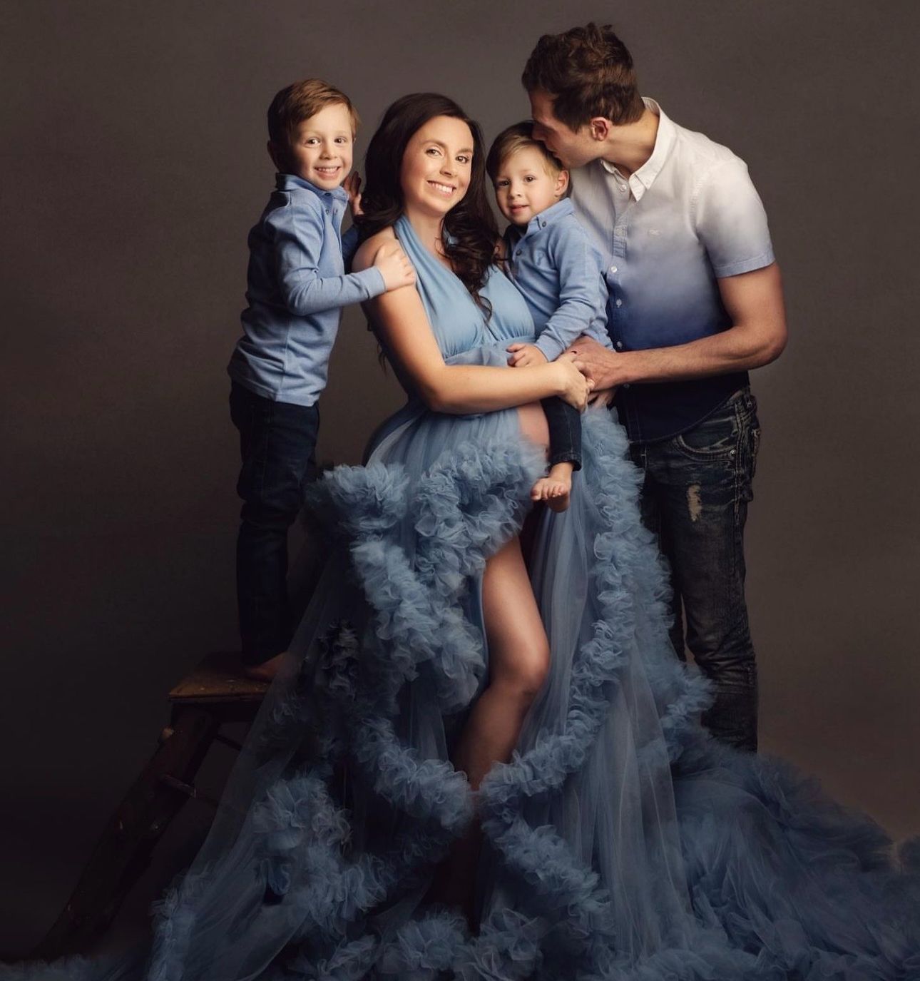 Pregnant woman in blue tulle gown poses with husband and two children for elegant maternity family portrait.