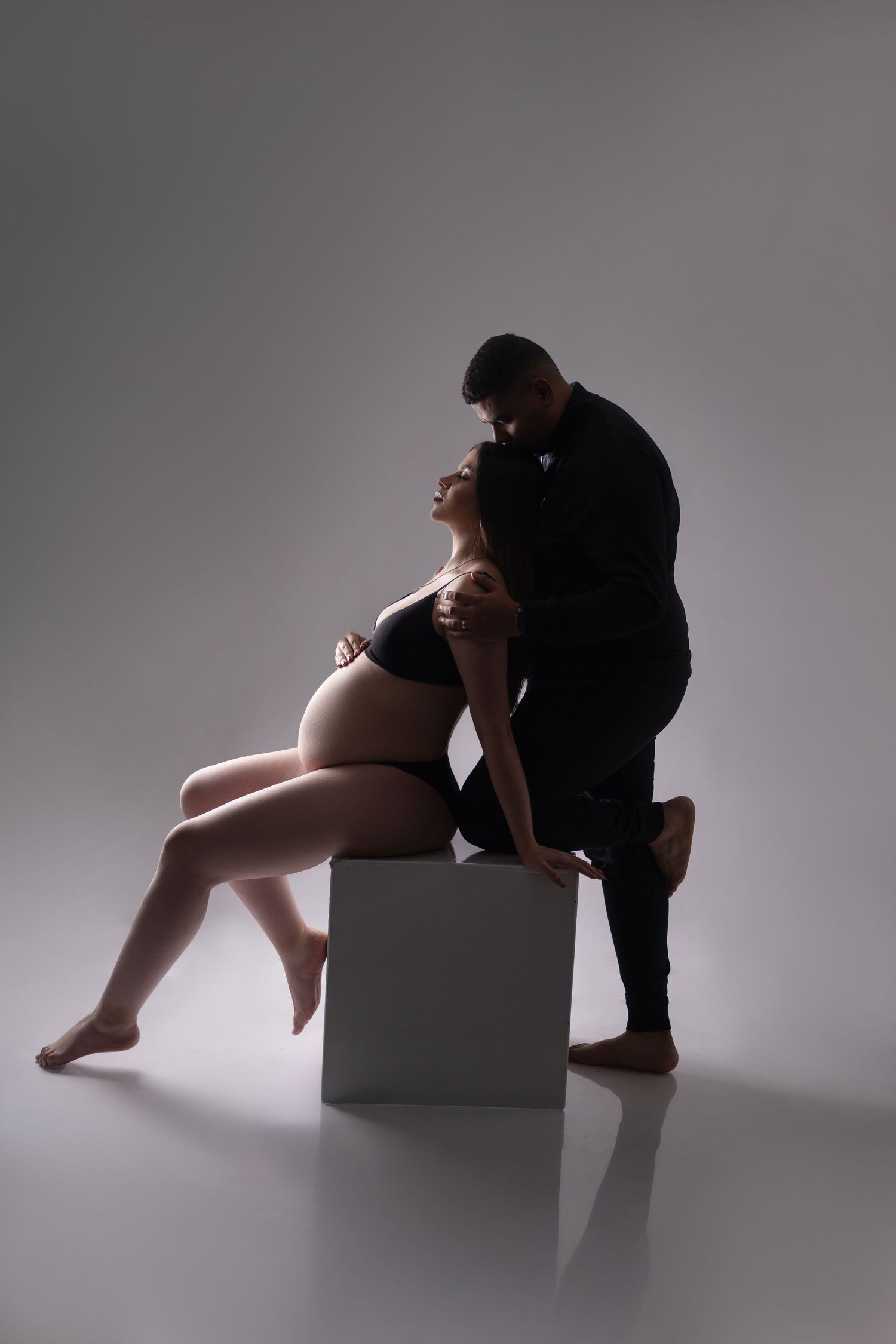 Intimate silhouette of couple during maternity photoshoot with studio lighting.