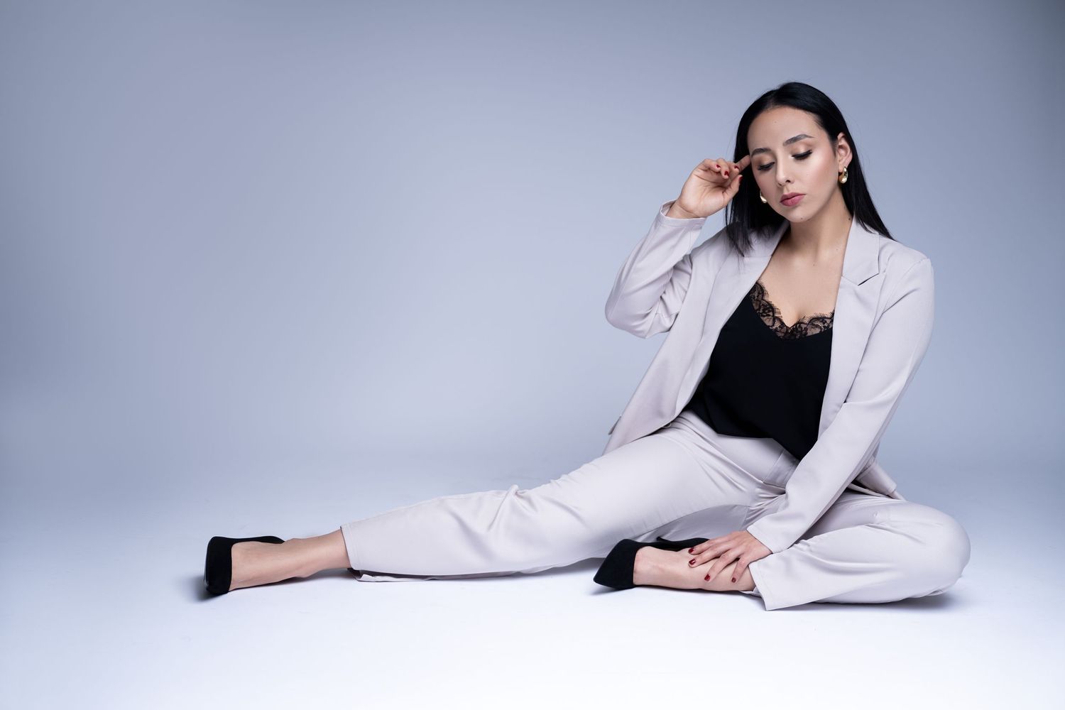 Model in light colored pantsuit reclining elegantly against studio background.