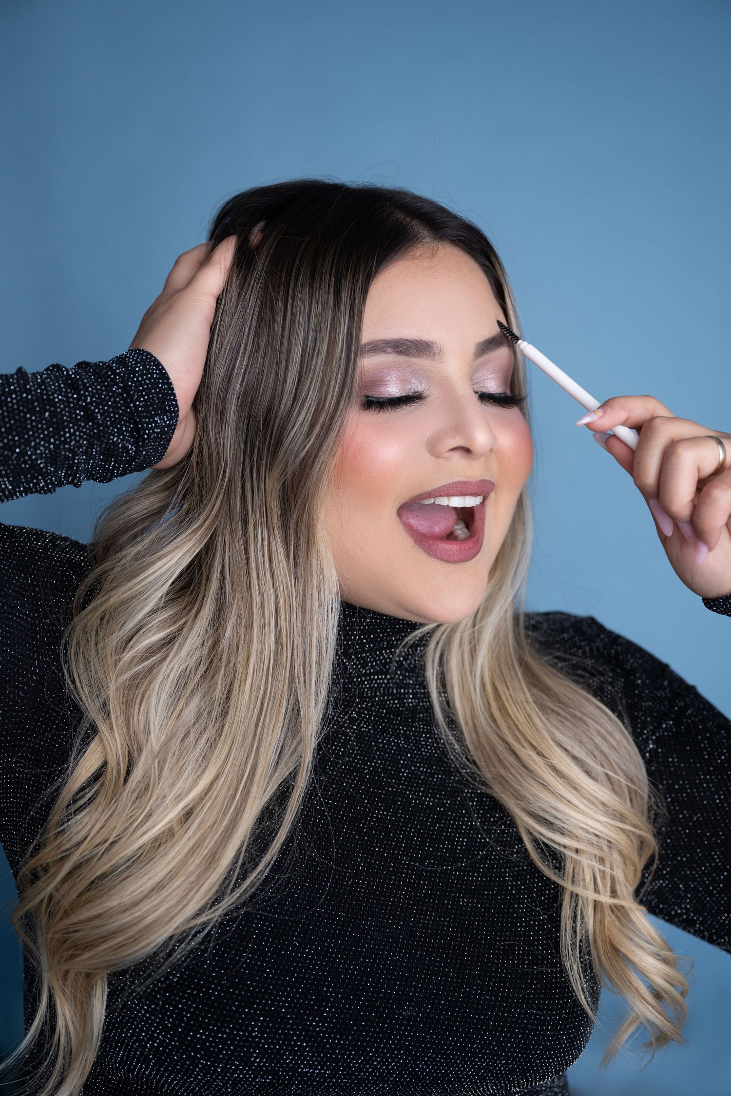 Beauty portrait showing makeup application with blonde ombre hair against blue background.