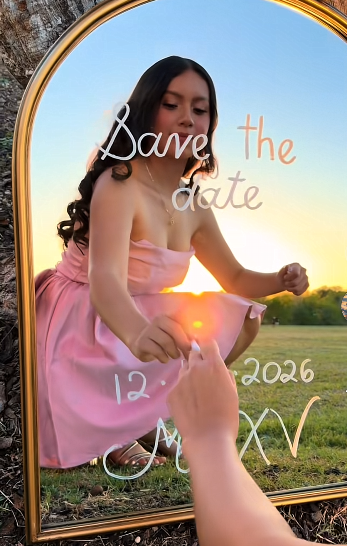A young woman in a pink strapless dress poses in a gold arch mirror for a Quinceañera Save the Date 2026.