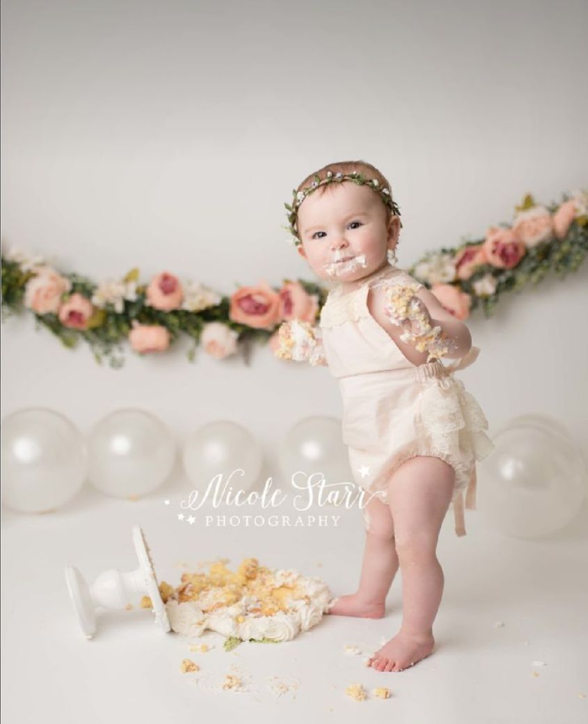 Sweet first birthday cake smash photo shoot with pink roses, white balloons and a destroyed cake on the floor.