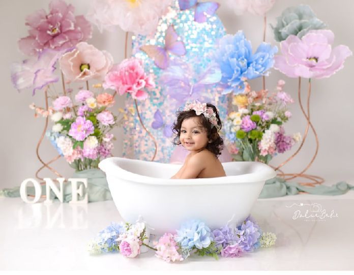 Dreamy bathtub scene decorated with pink and blue flowers, pastel colors, and glowing lights for a whimsical first birthday photo.