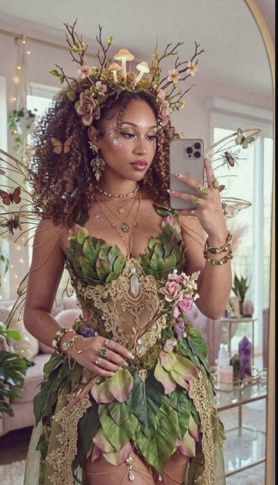 Woman in elaborate forest fairy costume with leaf dress, floral antler crown, butterfly wings, and jeweled accessories.