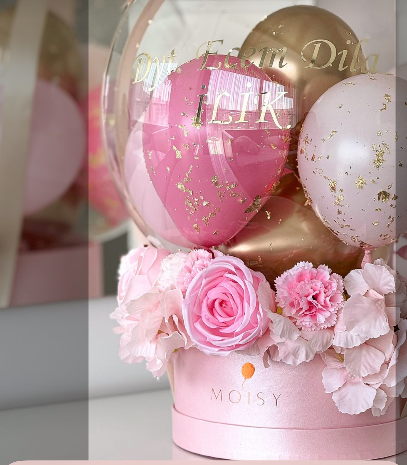 Pink floral arrangement with gold and pink balloons in MOISY branded box centerpiece.