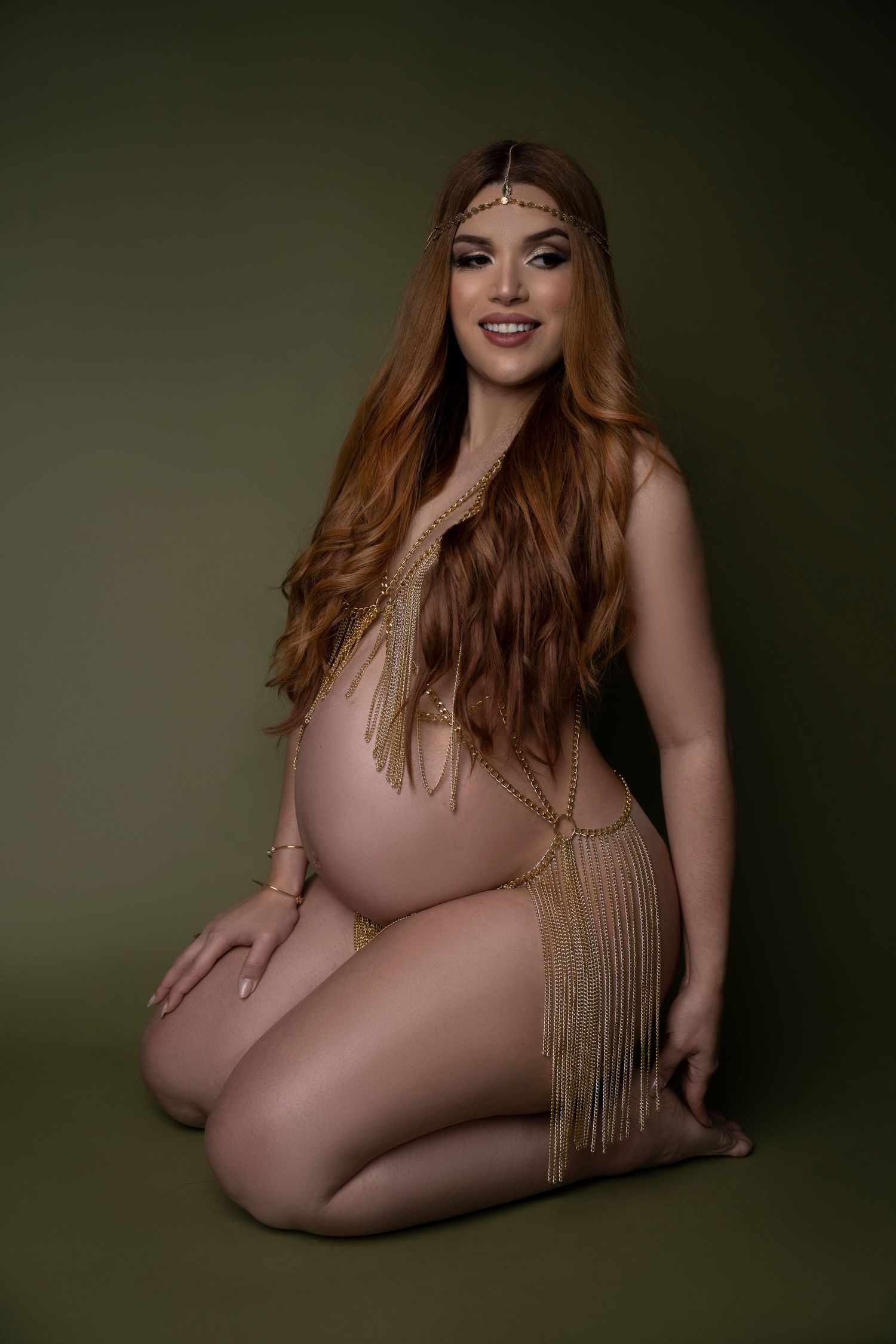 Maternity boudoir photo with golden fringe details and long flowing hair against dark background.