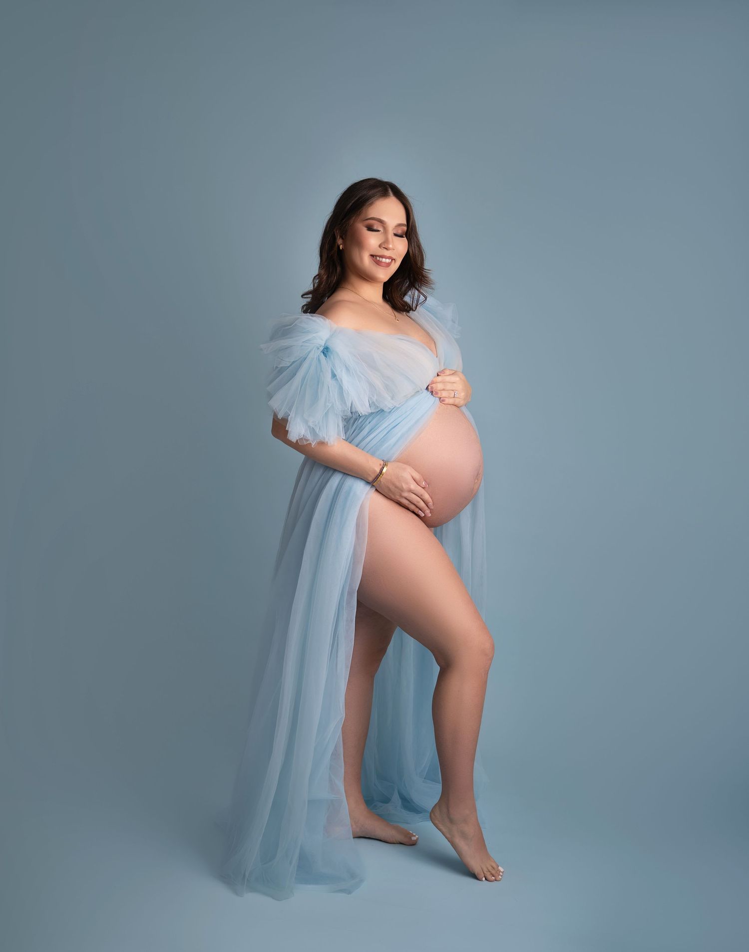 Ethereal pregnancy photo featuring light blue flowing fabric against blue-gray backdrop.
