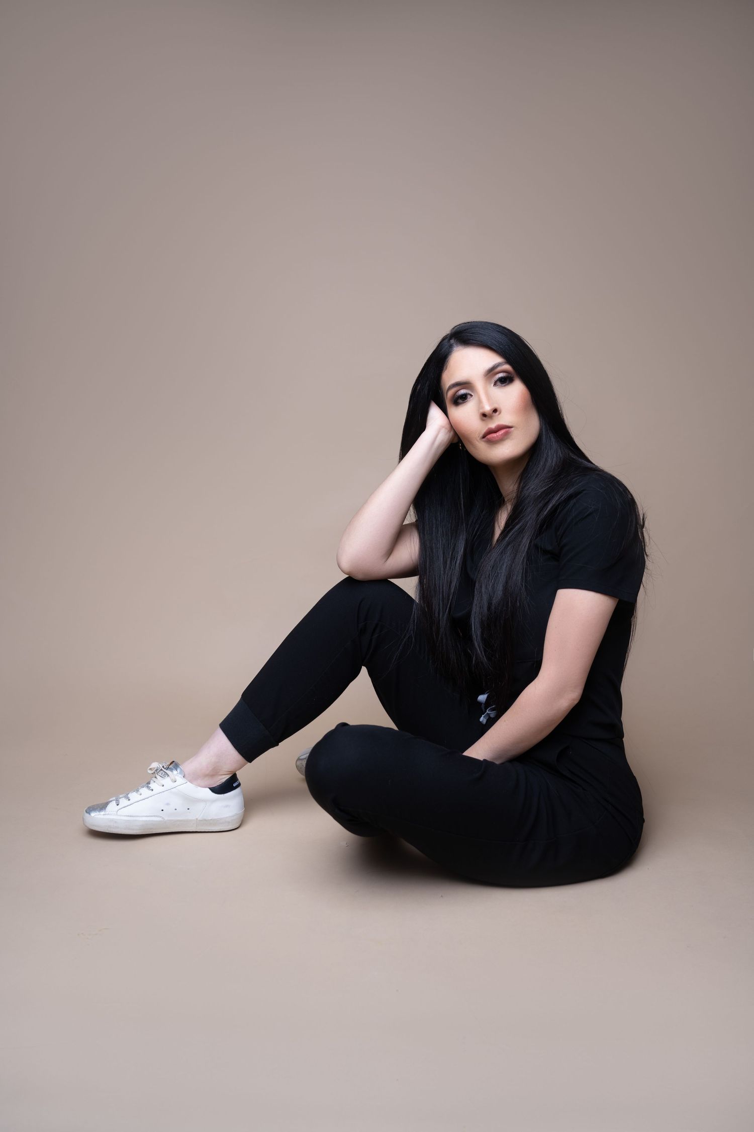 Casual studio portrait in all black attire with white sneakers against neutral backdrop.