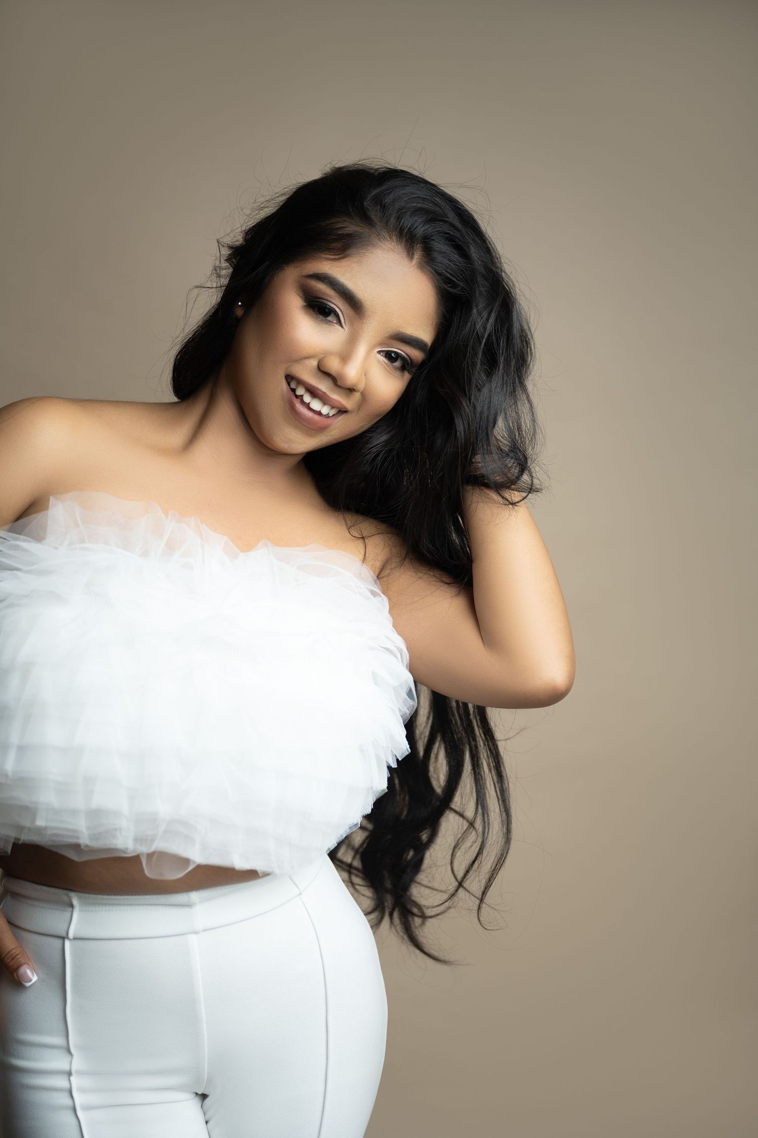 Studio portrait in white ensemble with long flowing dark hair against neutral background.