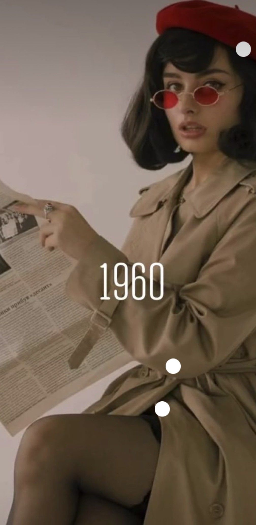 Woman in 1960s style outfit wearing red beret, oval sunglasses, and trench coat, holding newspaper.