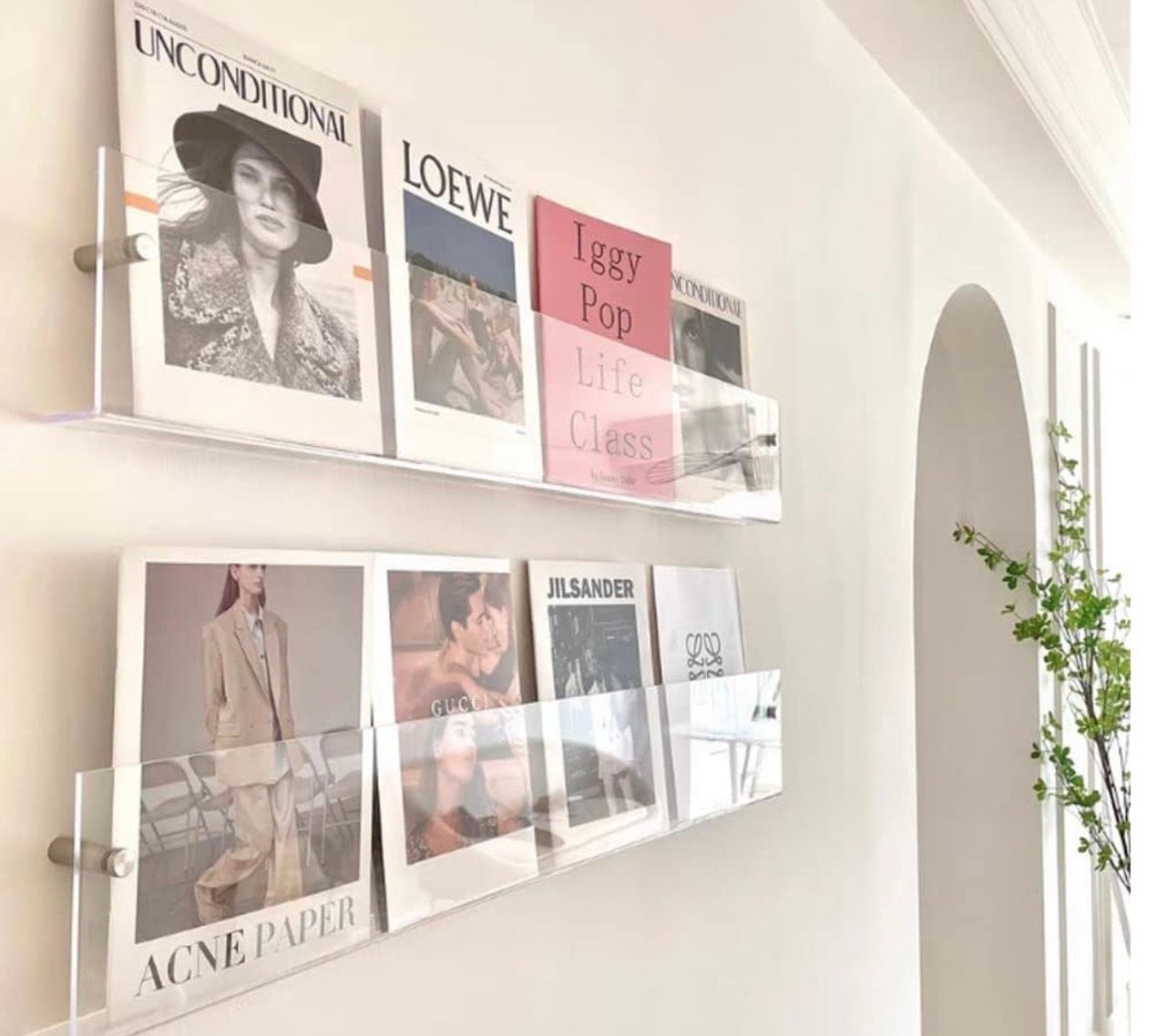 Two clear acrylic wall-mounted shelves displaying fashion magazines including Loewe, Acne Paper, and Unconditional.