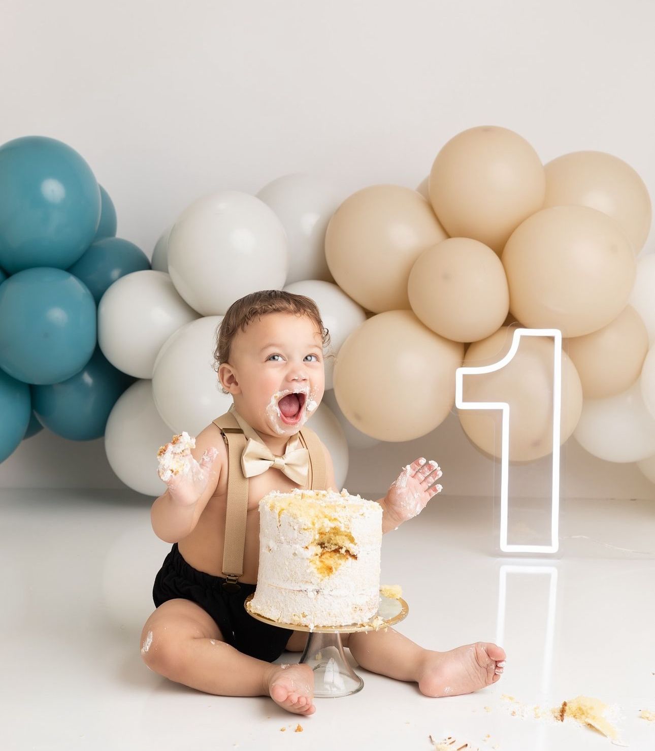 A joyful cake smash photo with blue, white and beige balloon decorations and a large number 1 display.