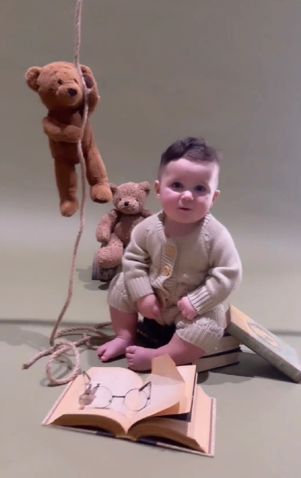 A sequence of images showing a baby and teddy bear puppet interacting with an open book on the floor.