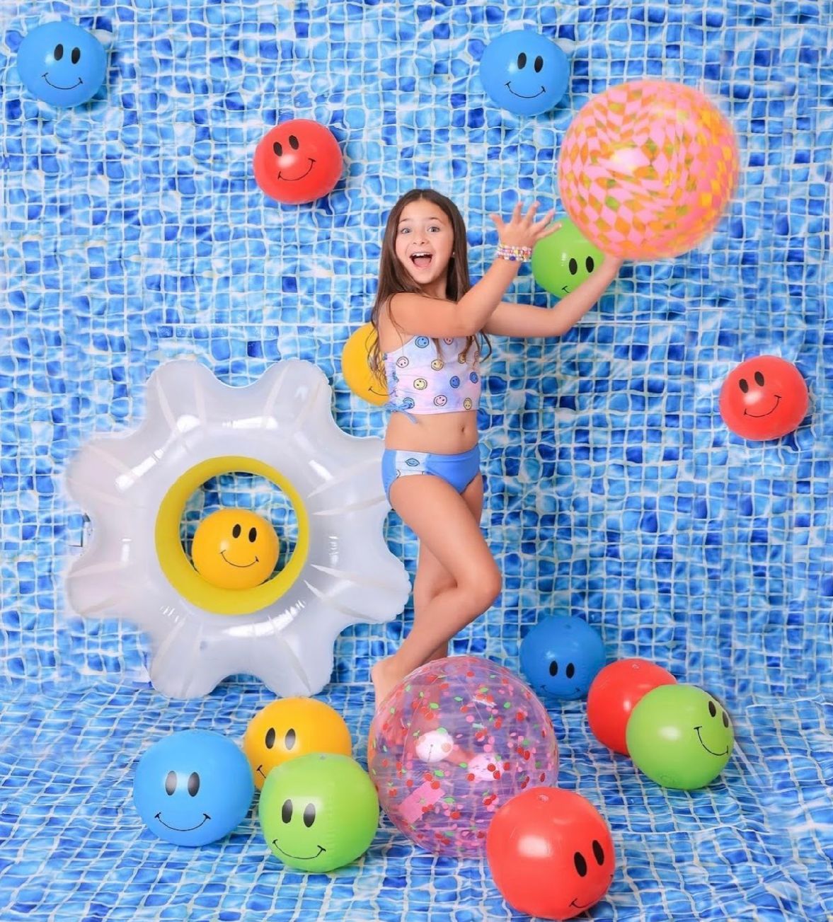 Colorful pool scene with blue mosaic tiles, inflatable toys and floating rings creating a playful summer atmosphere.