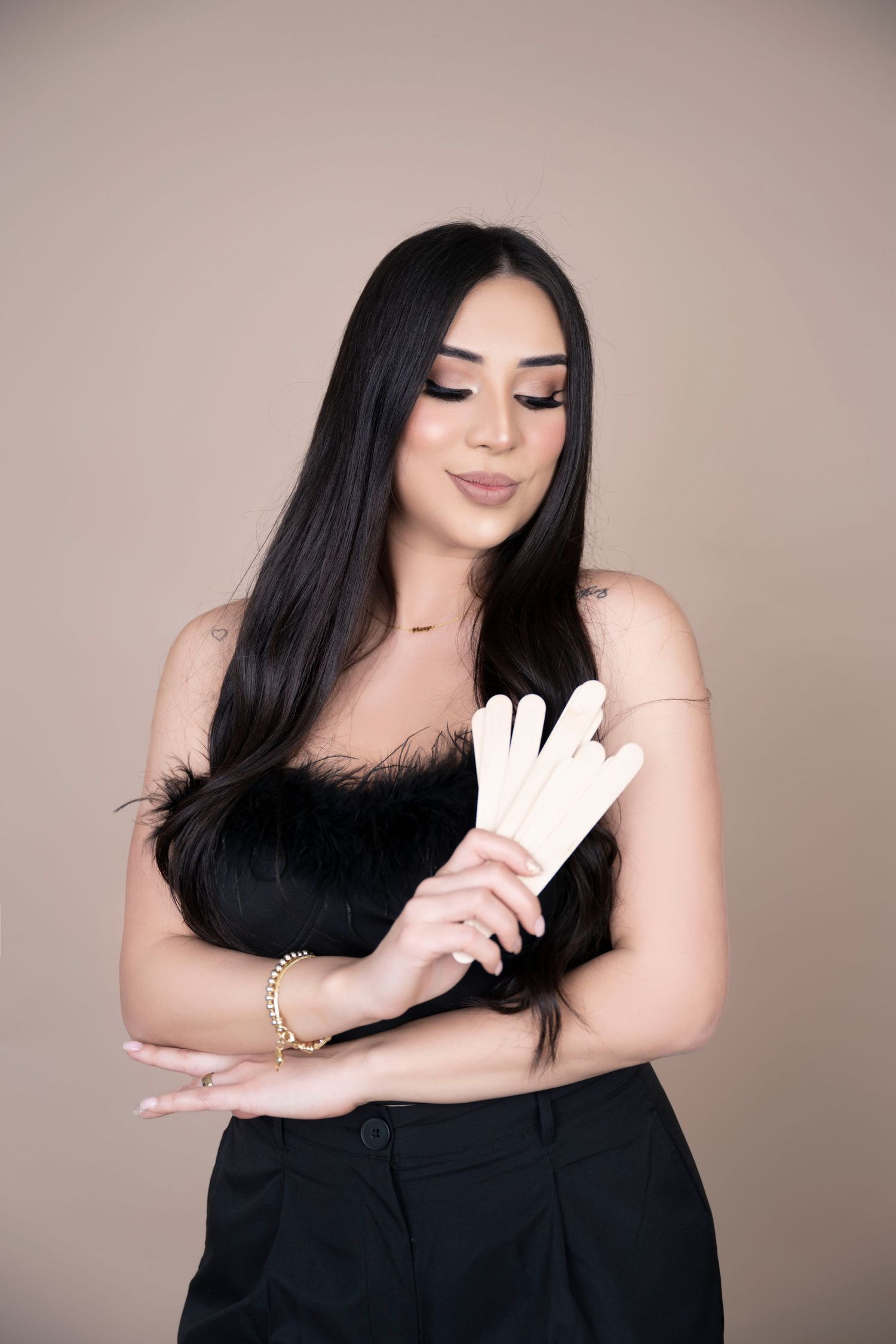 Woman in black outfit with long dark hair putting on white gloves against beige background.