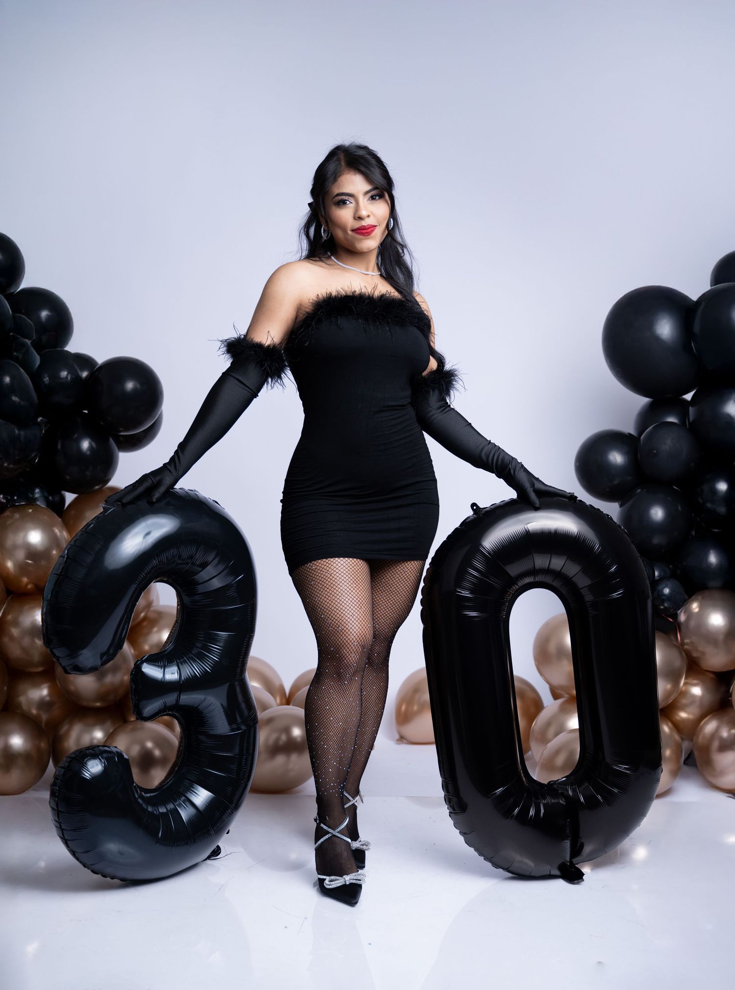 Glamorous birthday setup with black dress and balloon numbers against grey background.