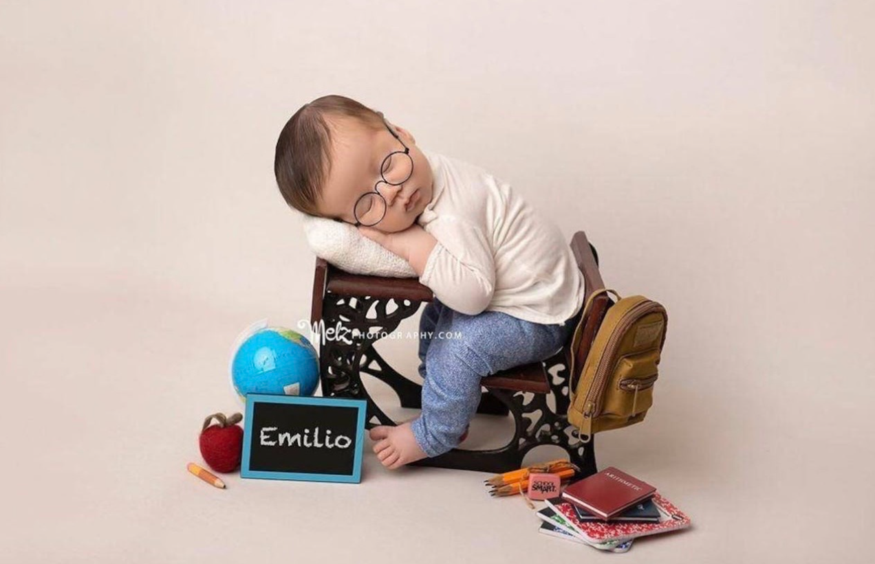 Small child sits on wooden prop with blue balloon and chalkboard sign during professional photo session.