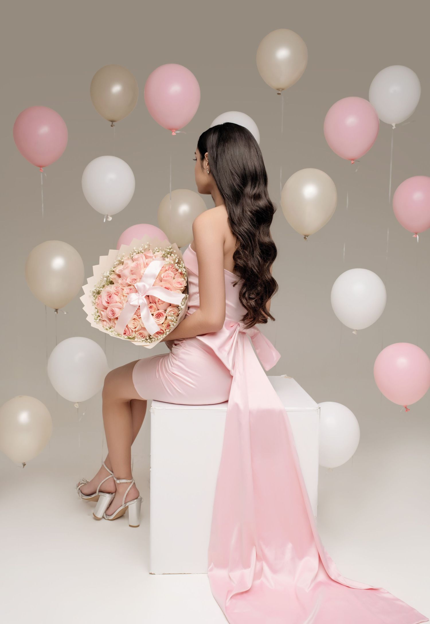 Pink and white balloons create a dreamy backdrop for a romantic maternity photoshoot in soft pastel tones.