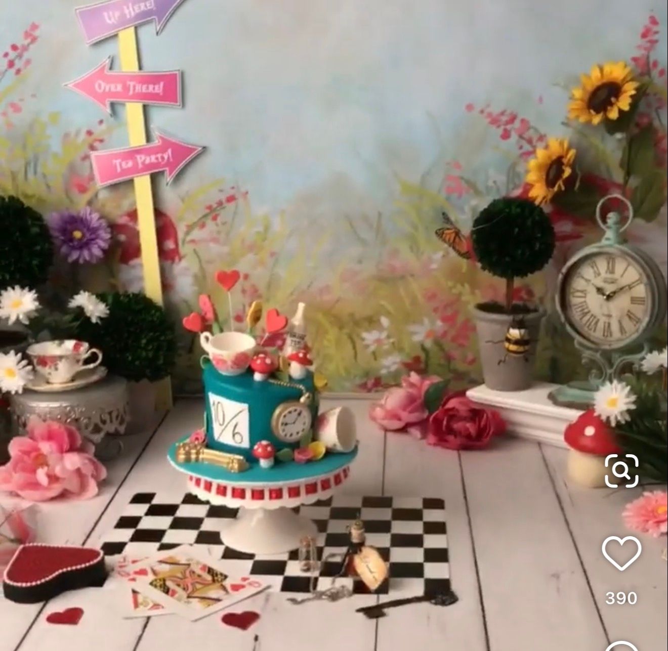 Alice in Wonderland themed cake smash setup with a clock-face cake, tea cups, playing cards, sunflowers and a checkered floor.