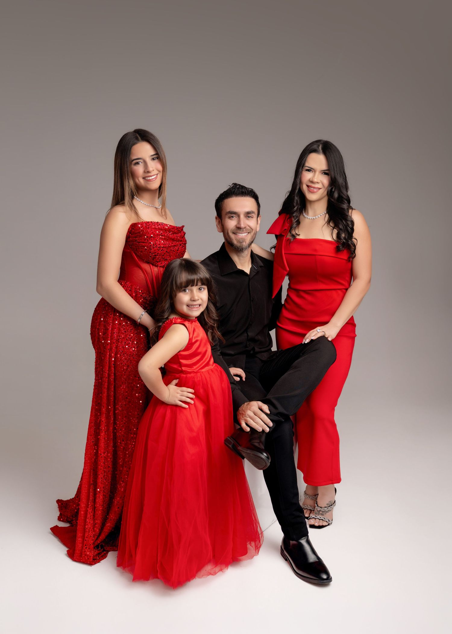 Family of four posing in red outfits for a professional studio portrait photo.