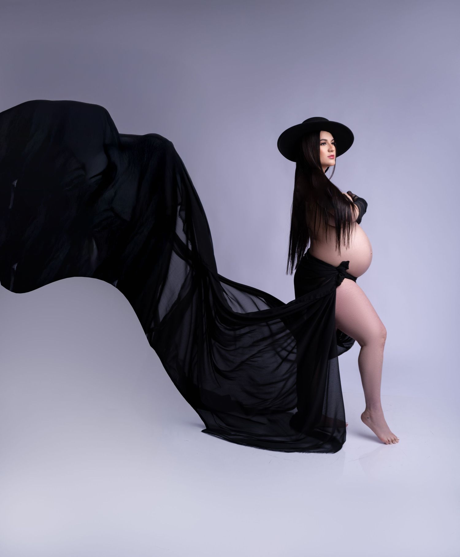 Dramatic maternity portrait with billowing black fabric creating movement against purple background.