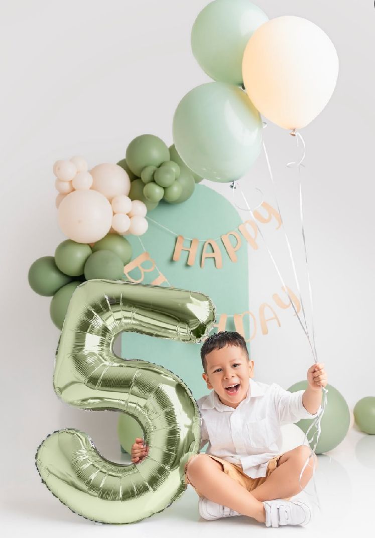 Birthday photoshoot with mint green number 5 balloon, pastel balloon arch, and happy celebrant in white.