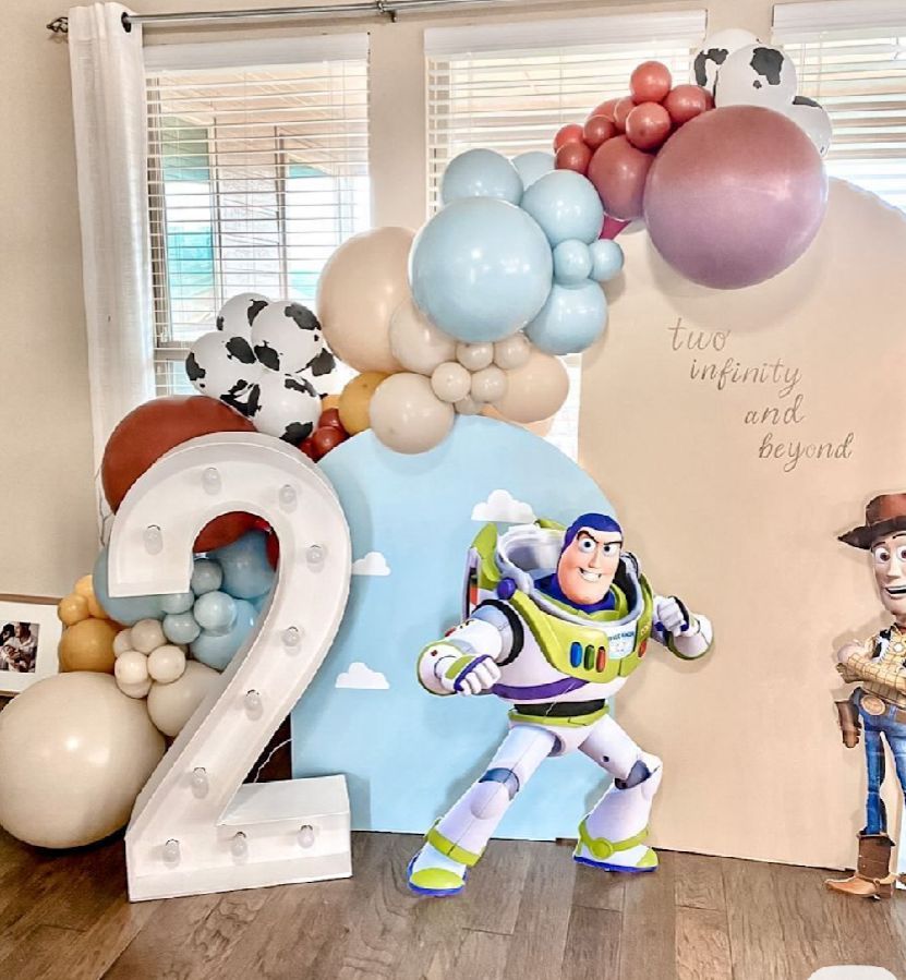 Pastel balloon decorations with Toy Story character cutouts arranged against a white wall.