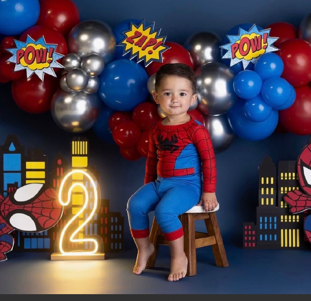 Superhero themed birthday setup with neon number 2, balloons, and cityscape backdrop.