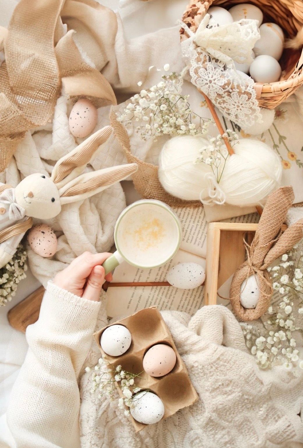 Cozy Easter flat lay with decorative eggs, bunny ornaments, baby's breath flowers and warm coffee in neutral beige tones.