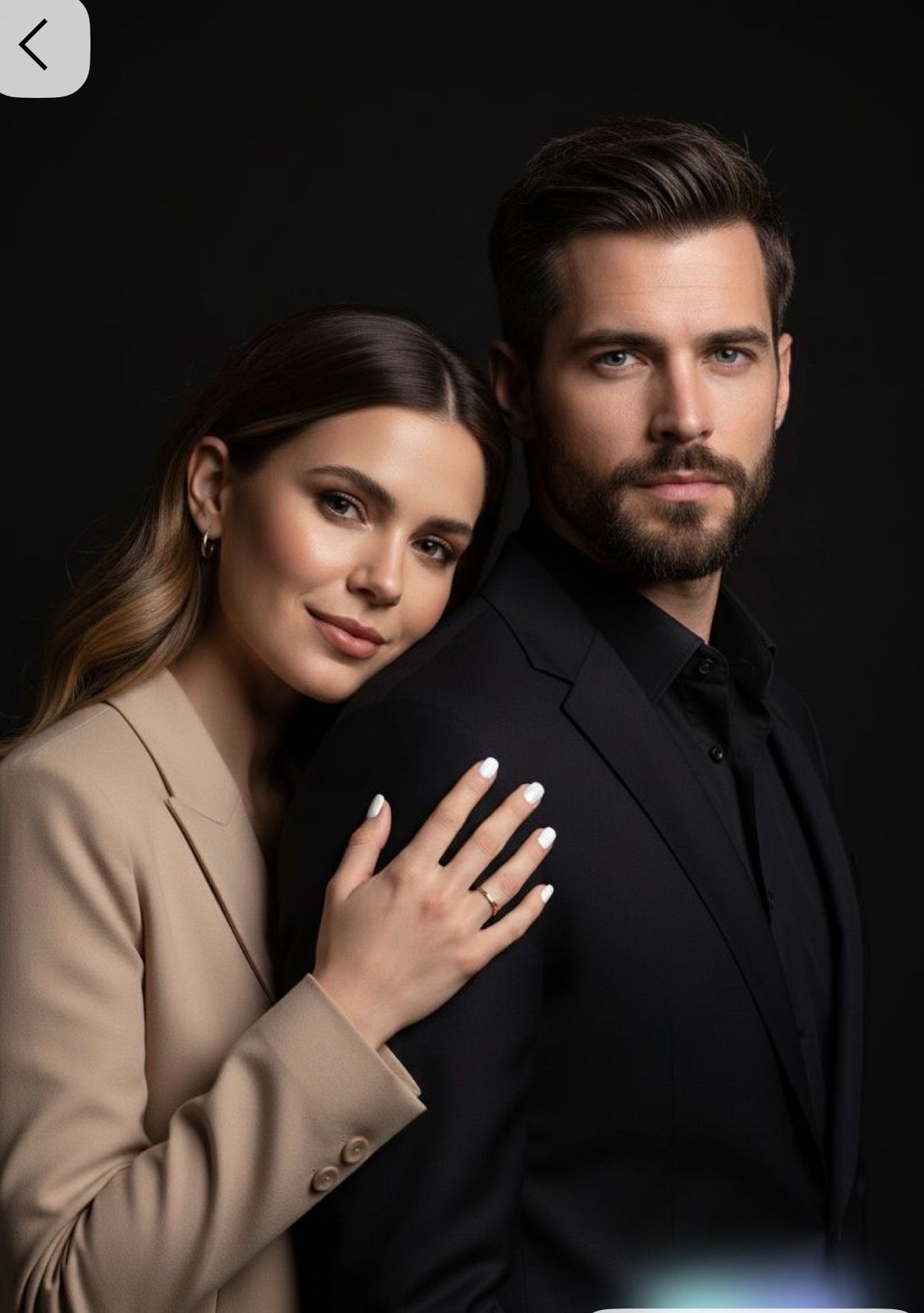 Elegant couple posing together, woman in beige blazer with ring, man in black suit, against dark background.