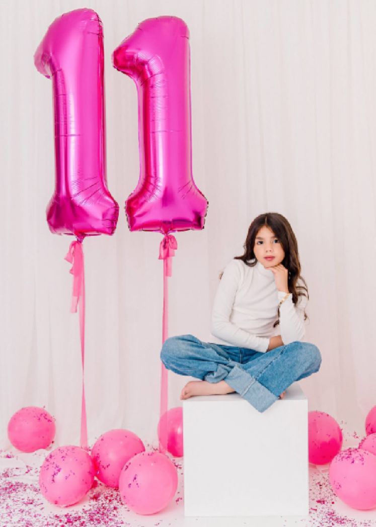 Pink balloon number decorations and confetti create a festive birthday setup against a white backdrop.