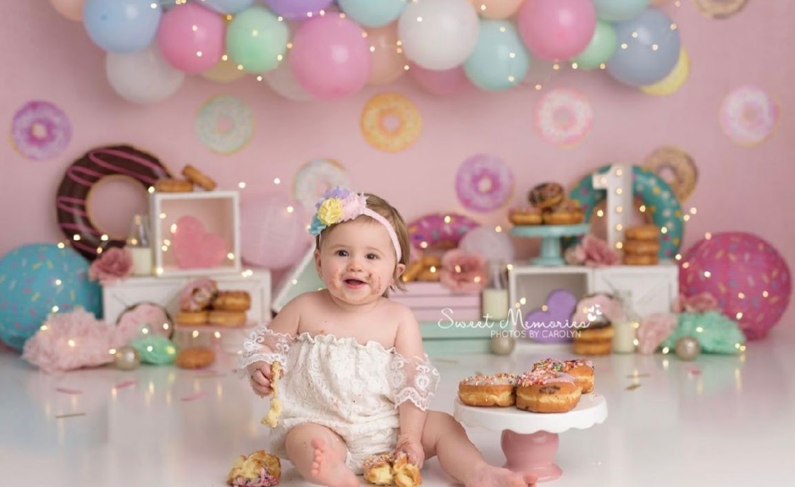 Festive first birthday party setup with pastel balloons, donuts and decorations in pink, blue and white colors.