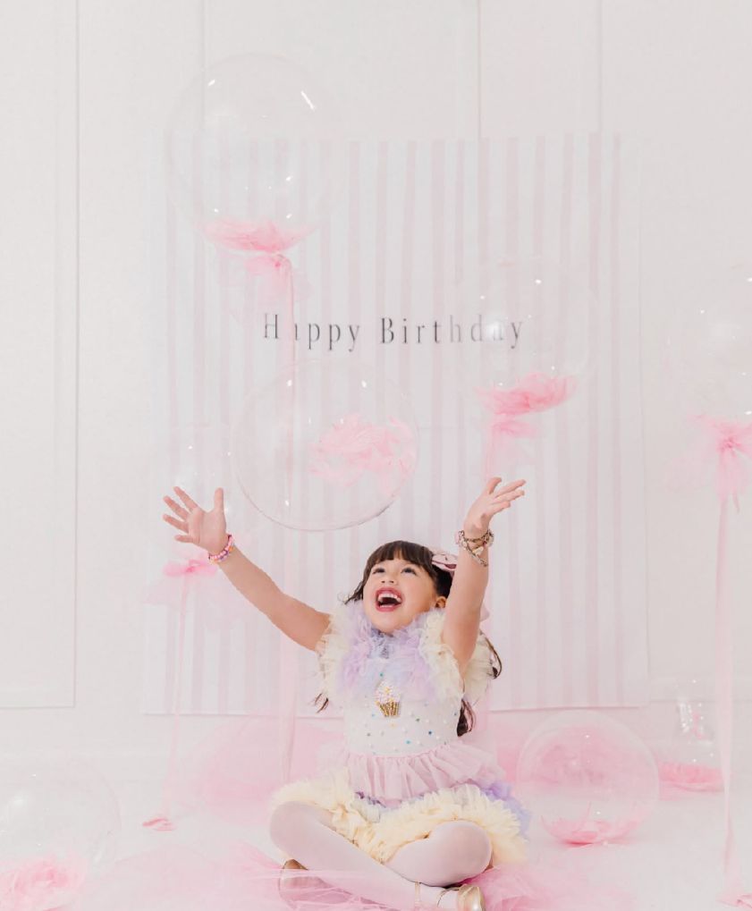 A joyful birthday celebration scene with pink feathers floating against a white striped backdrop.