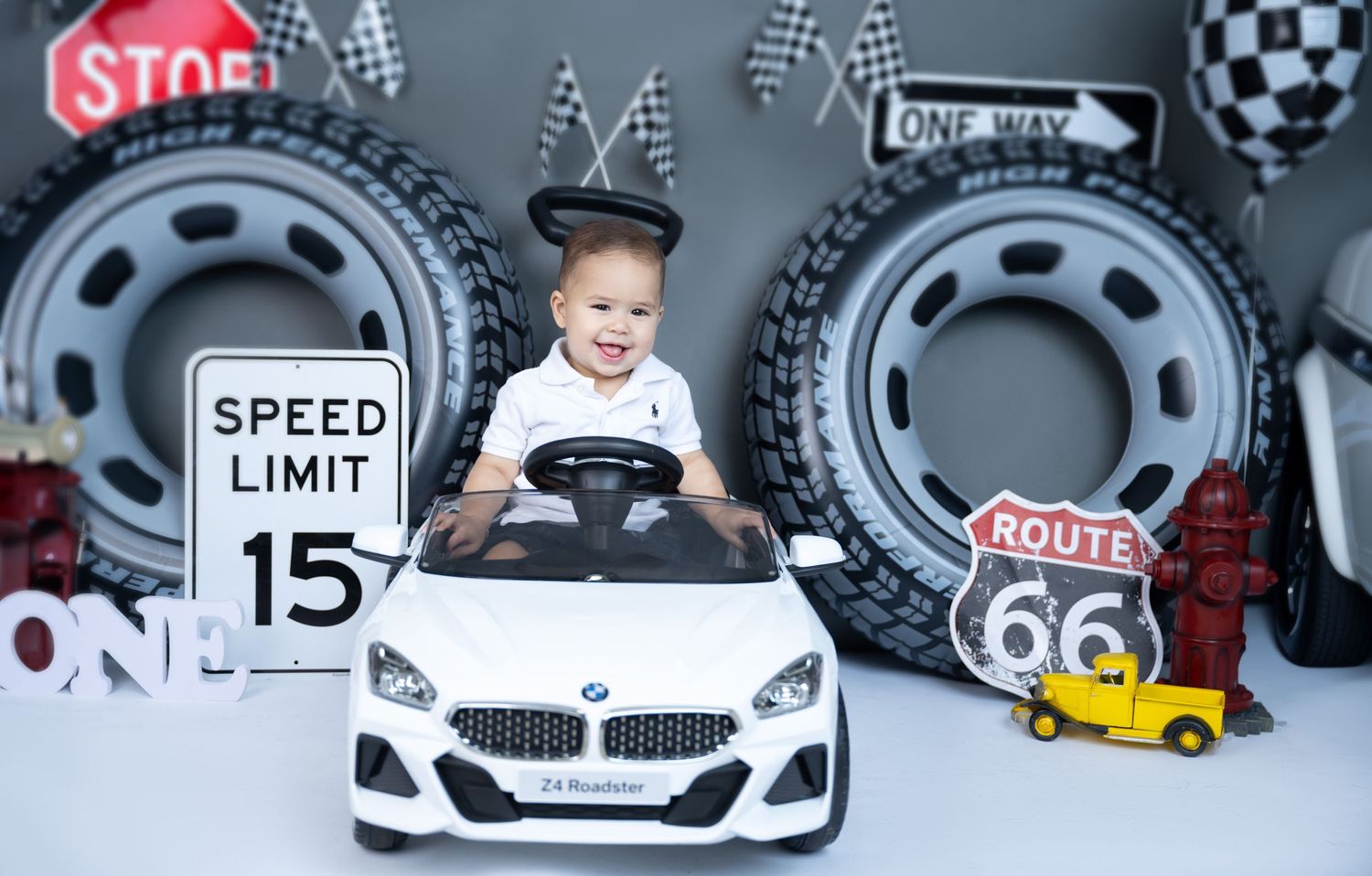 Baby driving toy BMW car in racing themed photoshoot with checkered flags.