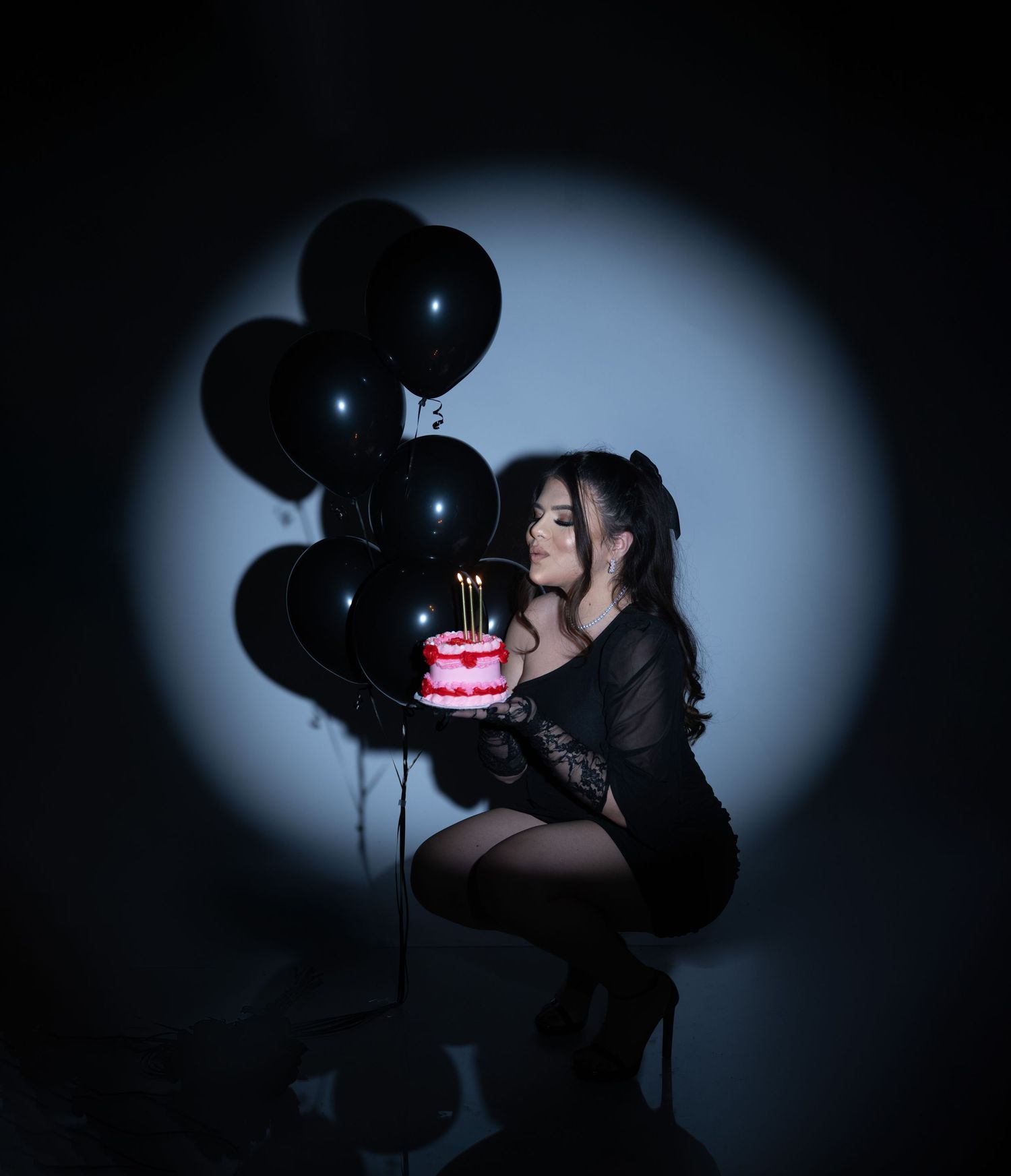 Moody portrait with black balloons and glowing cake in spotlight.