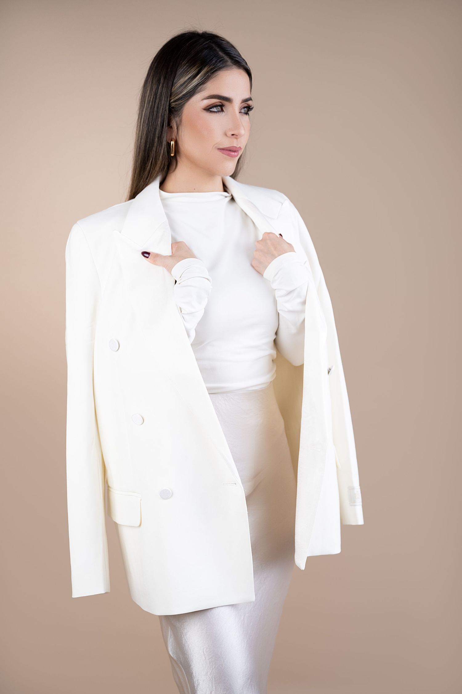 A model poses in an elegant all-white ensemble featuring a tailored blazer and fitted dress against a neutral backdrop.