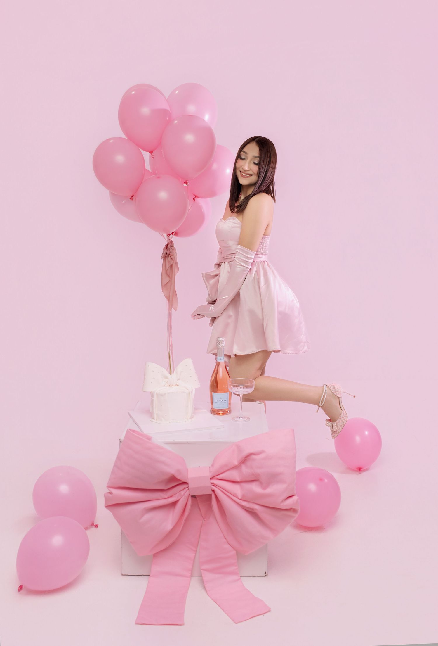 Pink balloons and a large bow create a romantic feminine scene against a soft pink backdrop.