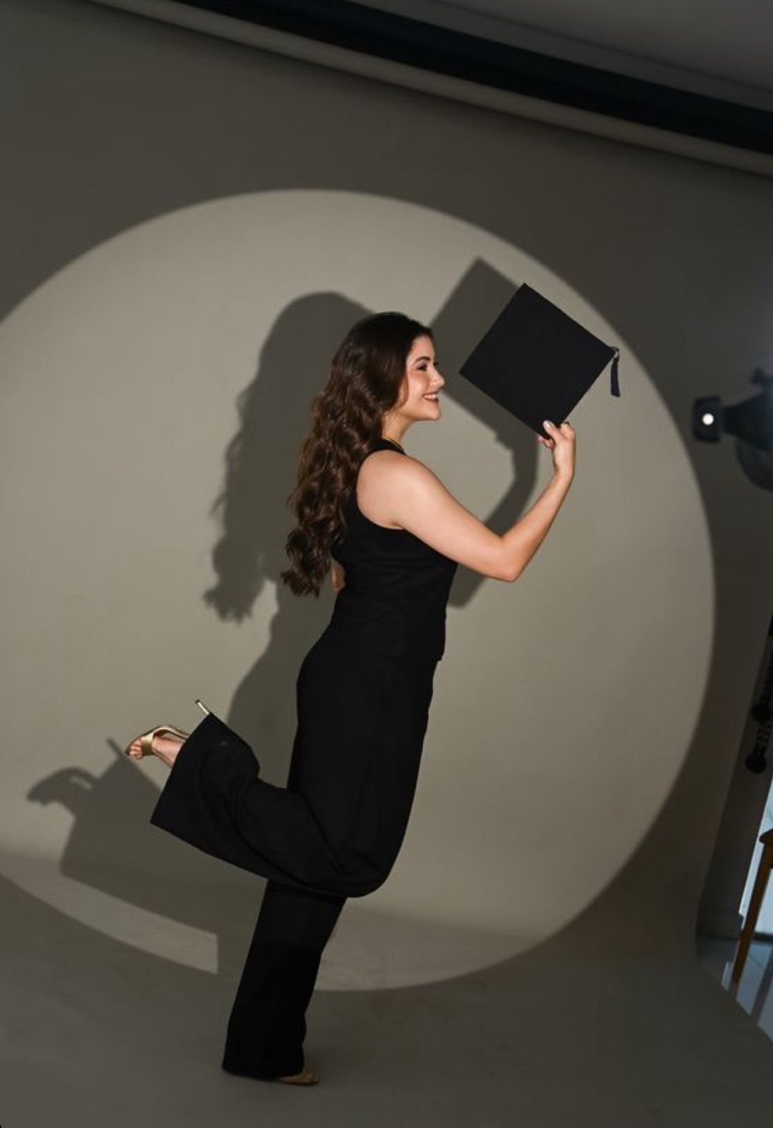 A person in a black dress poses artistically against a wall with a spotlight creating a dramatic circular shadow effect.
