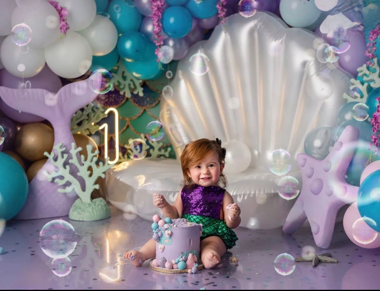 A dreamy baby photography setup with teal and purple balloons, bubbles, and soft lighting for a magical underwater theme.