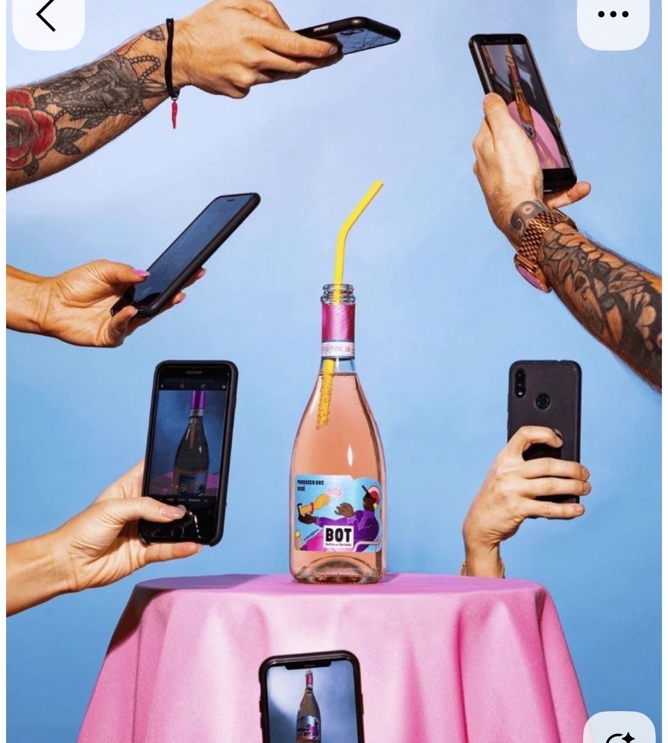 Multiple tattooed hands holding smartphones photograph a BOT rose wine bottle on a pink table.