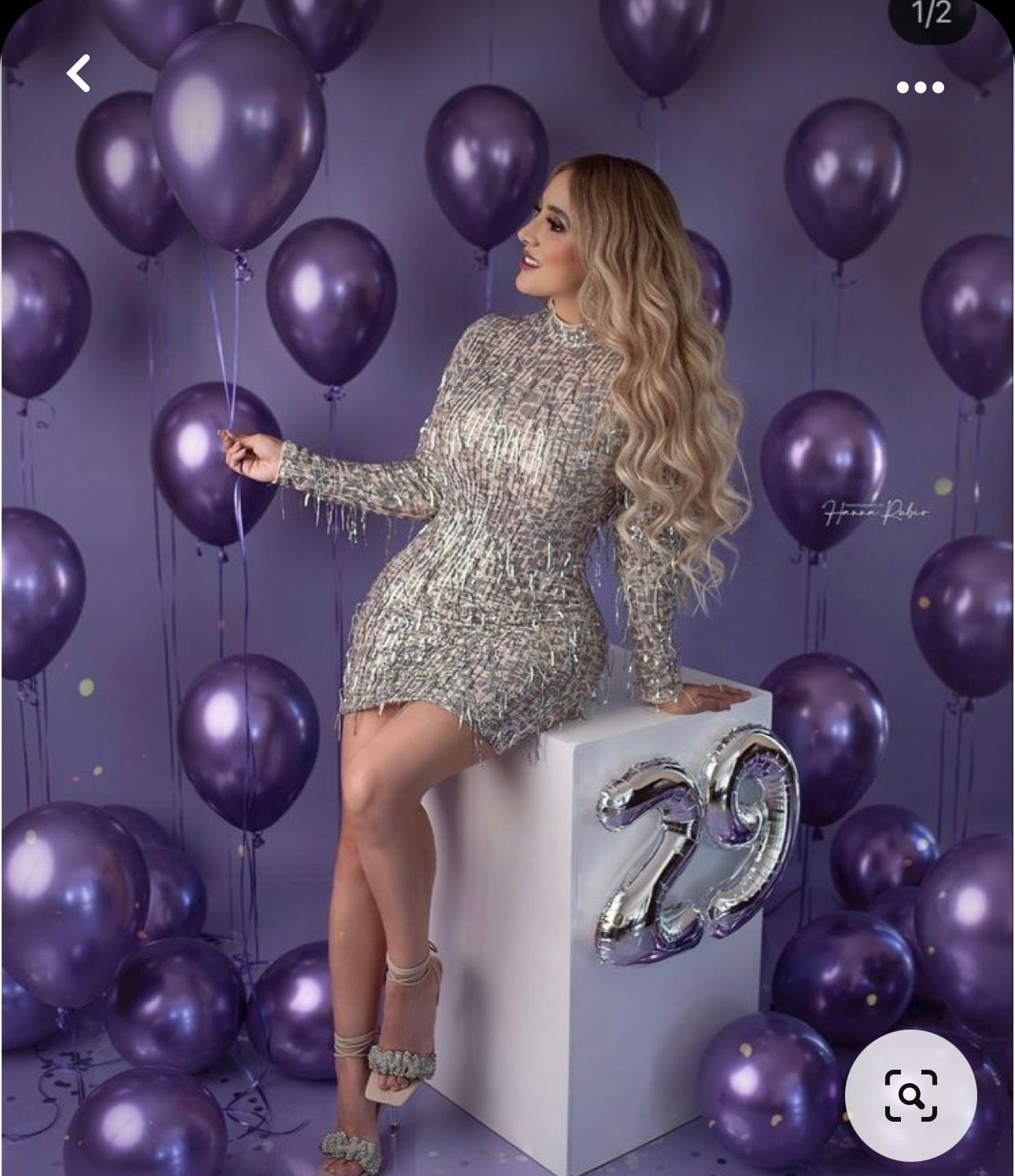 Woman in silver sequin mini dress poses with purple metallic balloons beside a white cube with number 29.