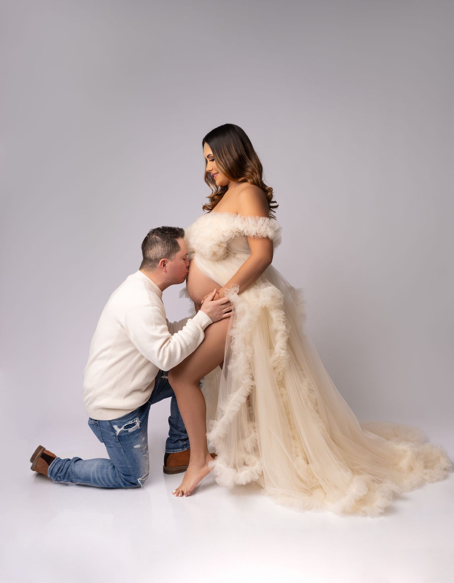 Intimate maternity portrait with couple in cream tones against neutral background.