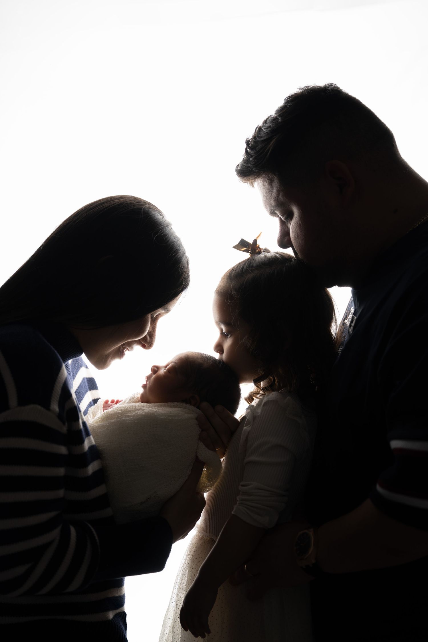 Silhouette of family sharing intimate moment with newborn in dramatic lighting.