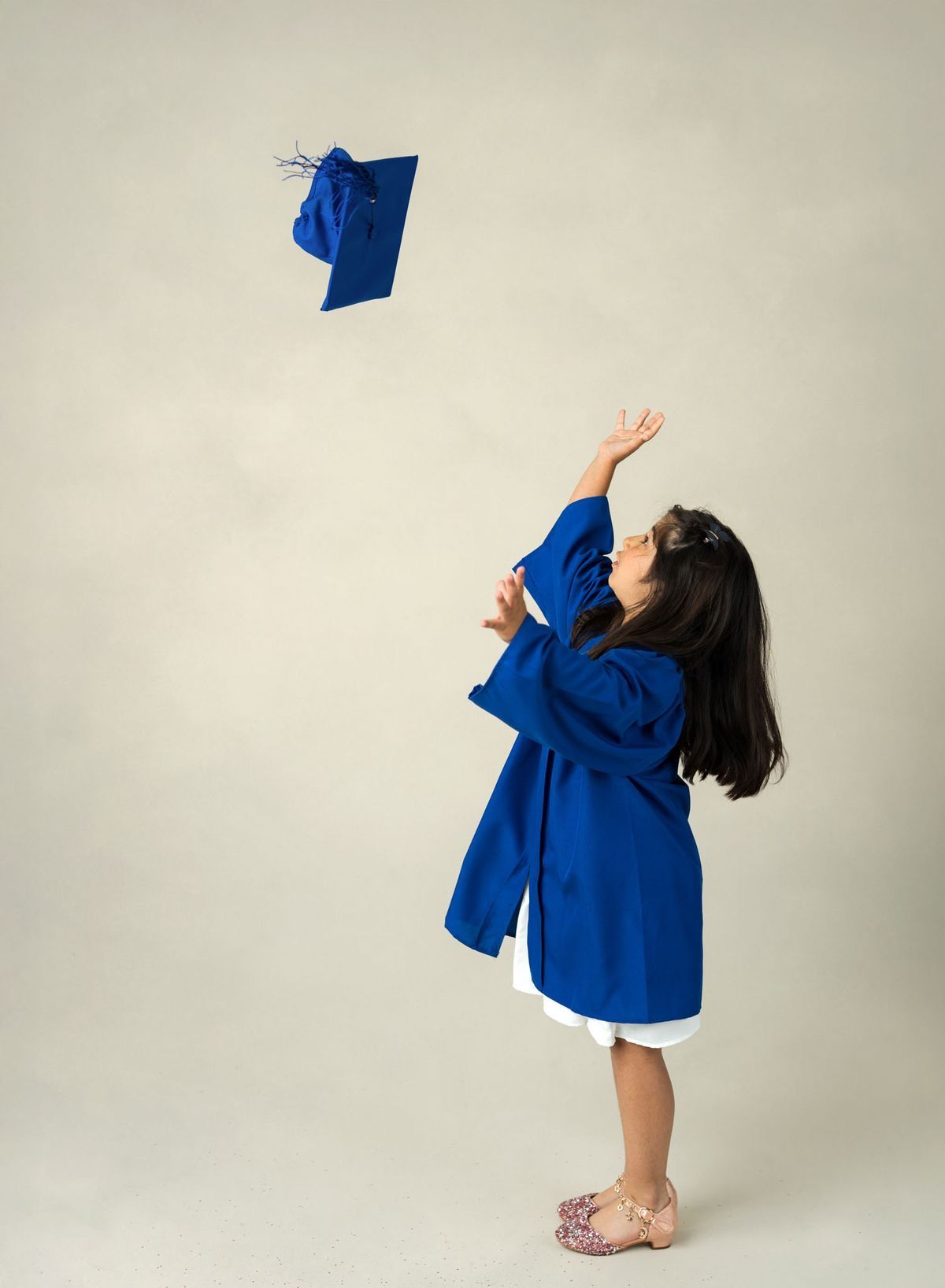 Young girl in blue graduation gown tossing her cap in the air, celebrating her kindergarten graduation.
