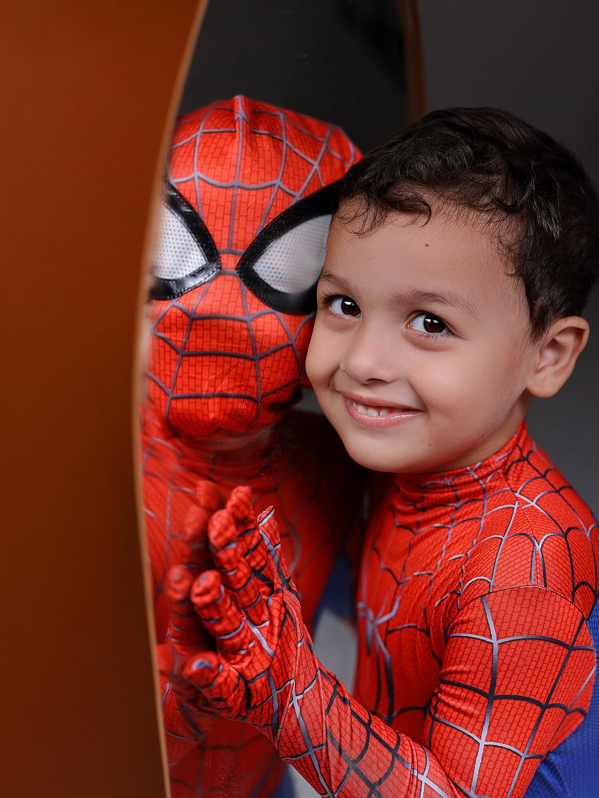 A smiling young boy in a Spider-Man costume poses cheek-to-cheek with a Spider-Man character in full red and blue suit.