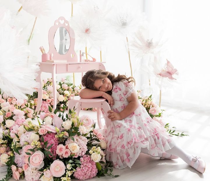 A newborn baby sleeps peacefully on a white backdrop surrounded by soft pink roses and delicate floral arrangements.