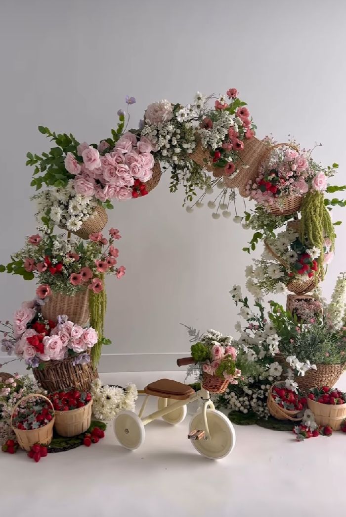 Romantic floral arch display with pink roses, baby's breath, and greenery arranged around a vintage white bicycle decoration.