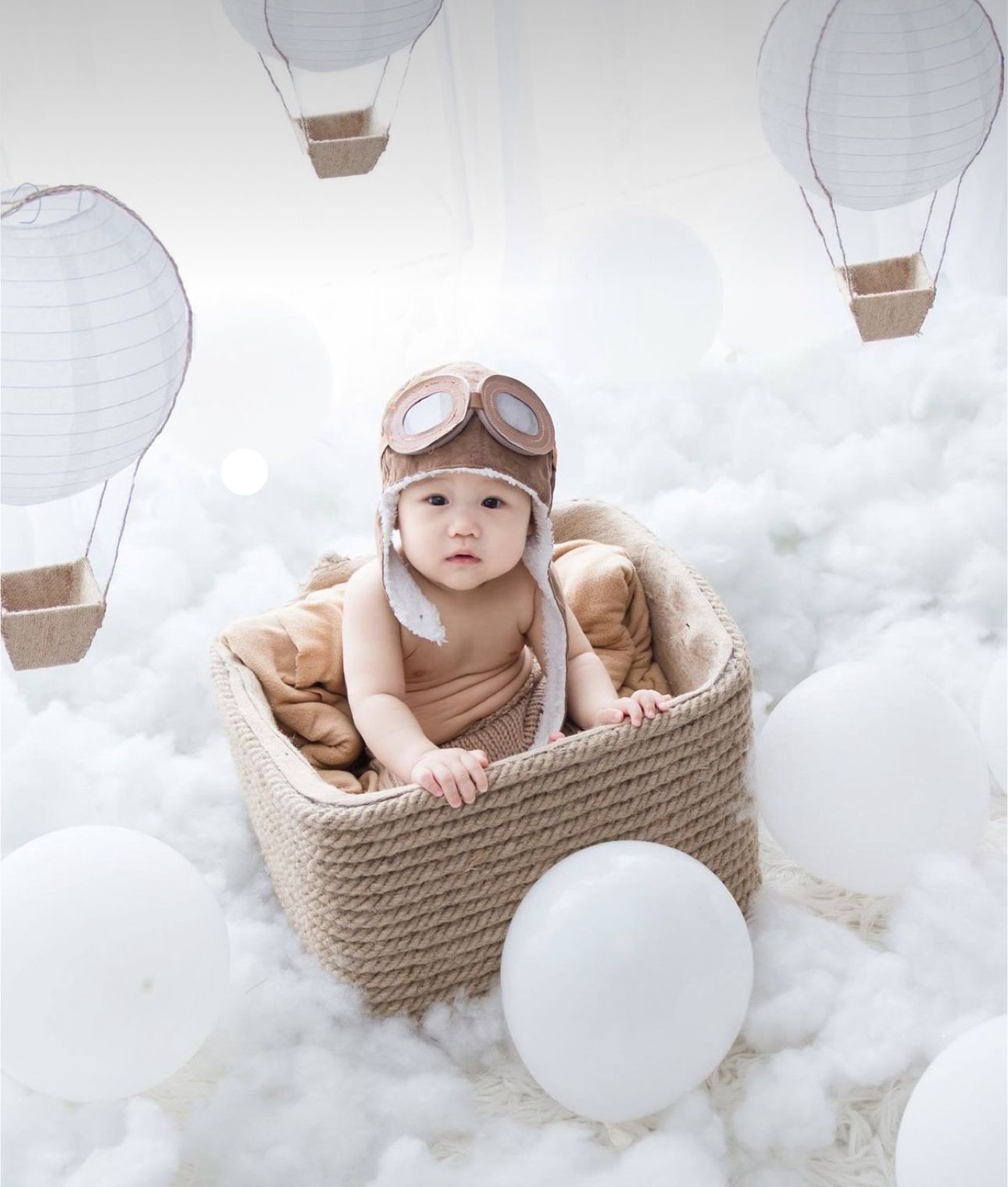 A dreamy nursery scene with a woven basket among white hot air balloon decorations and fluffy cloud-like textures.