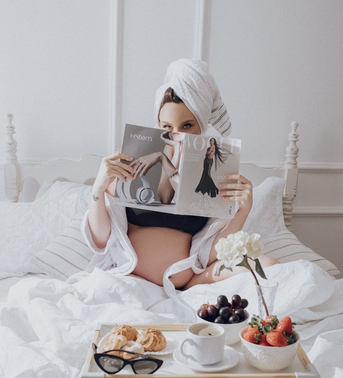 A cozy breakfast scene in bed with white linens, sunglasses, and fresh fruits arranged aesthetically.