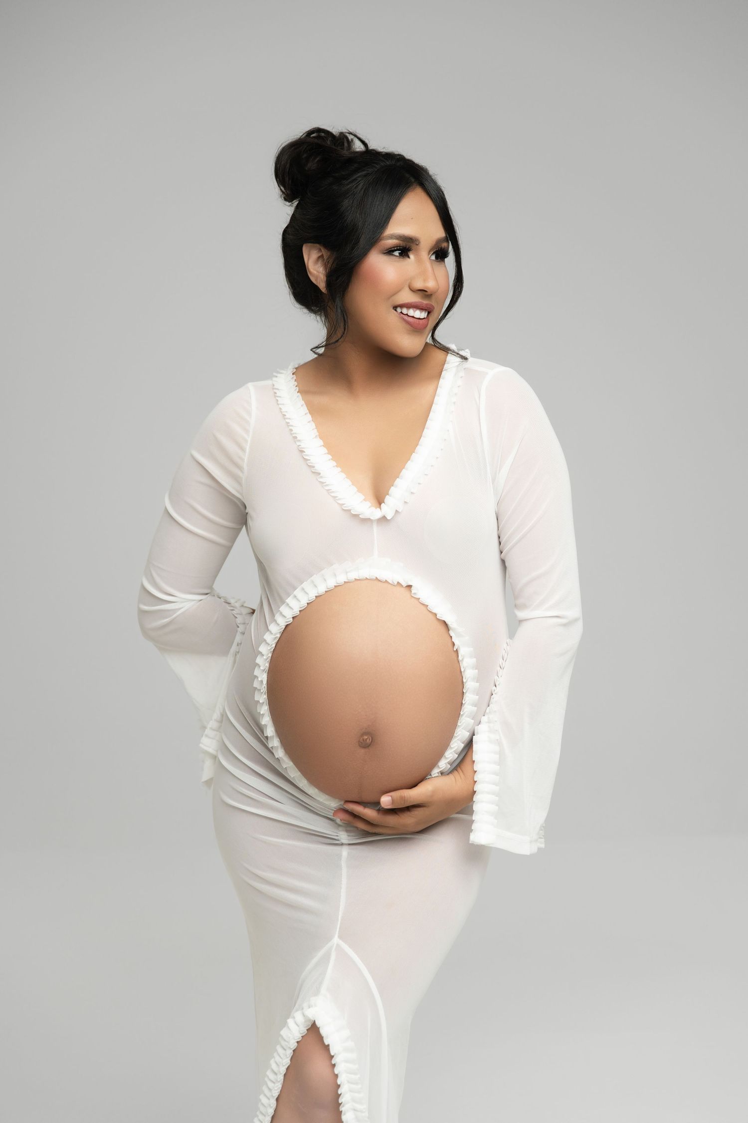 Maternity photoshoot series showing a pregnant figure in flowing white dress against grey backdrop.